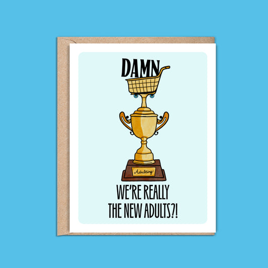 4.25 x 5.5” A2 size card illustration of gold grocery shopping cart trophy, light blue background. The text reads, "Damn We’re Really the New Adults". Blank inside. Black Woman Owned.