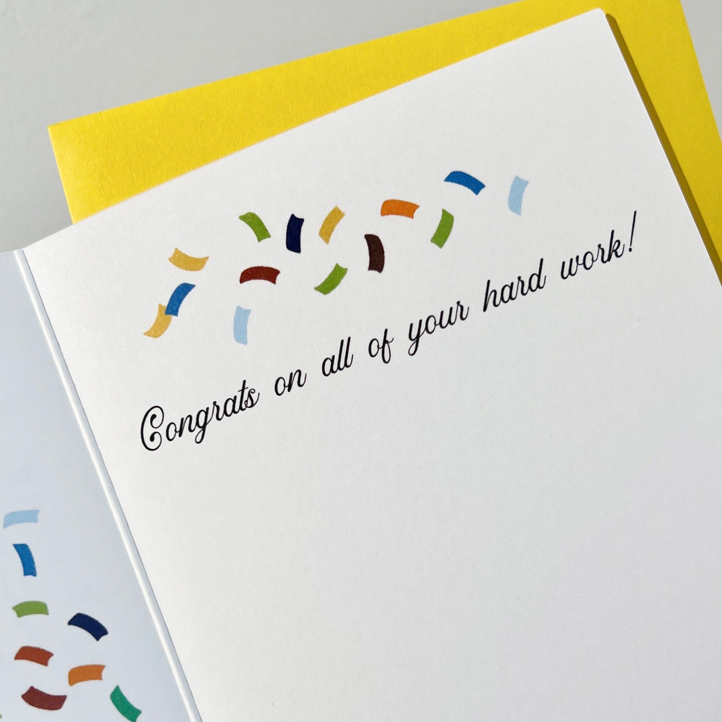 Inside of A2 size vibrant graduation card featuring colorful confetti and collegiate pennant banners. “Officially Alumni Status, Congrats Graduate!” text on the front with "Alumni” on the top burgundy banner and “Status!" below on a blue banner. Colorful confetti and a message inside the card. Envelope included.