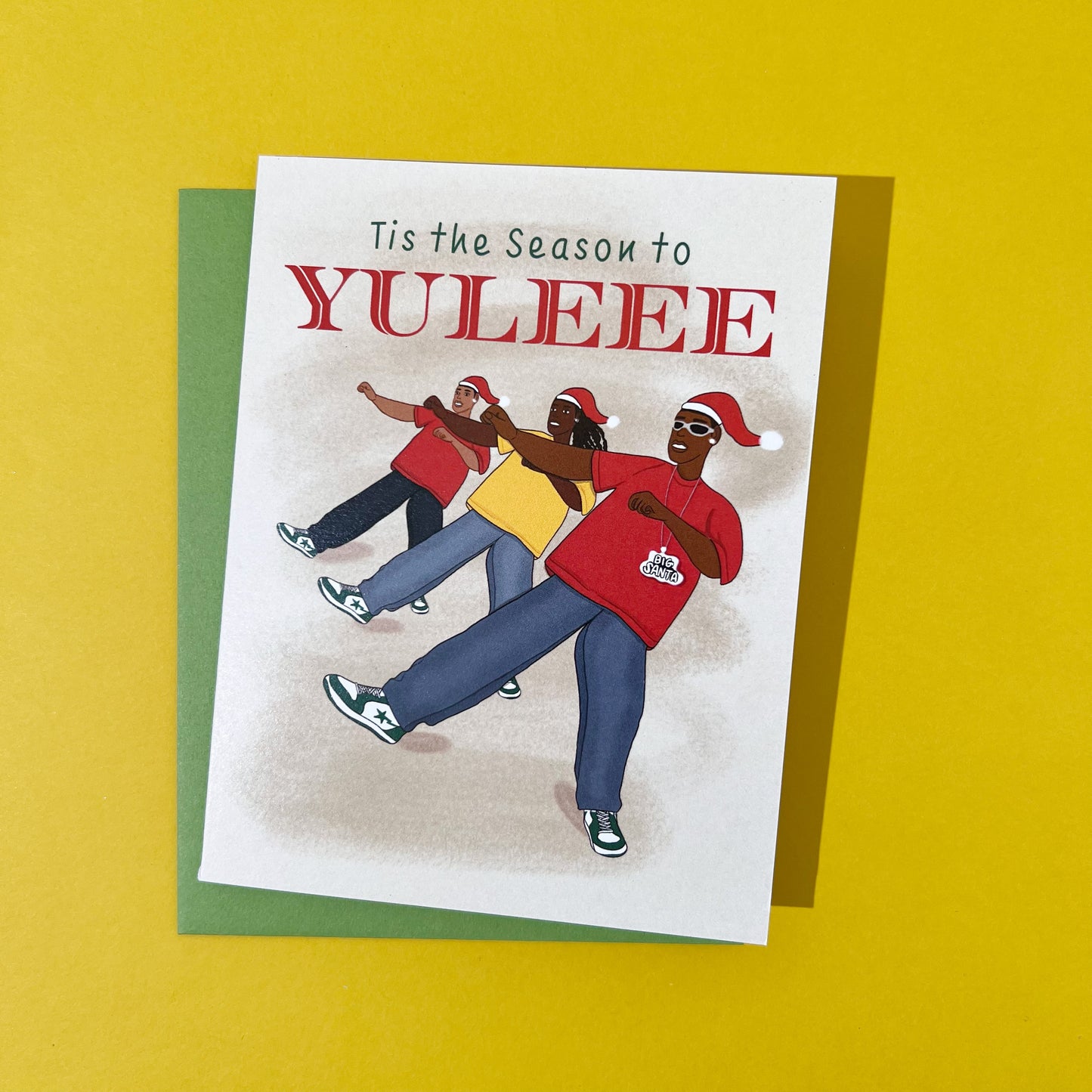 A2 card illustration of 3 guys dancing to Soulja Boy's song Crank Dat Soulja Boy; doing the Yule dance move with one foot off the ground and their arms across their chest, wearing Santa hats, red and yellow XL white tee’s, and baggy jeans, and blinged out diamond earrings. The first guy is rocking silver soulja boy Y2K glasses. At the top of the card are the words "Tis the Season to", in green and "Yuleee" in a red serif font. The inside of the card is blank. Envelope included. Black Woman Owned.
