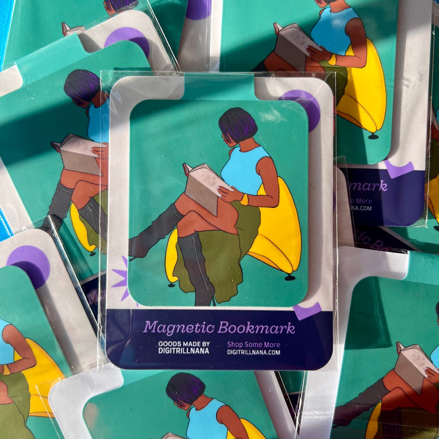 Magnetic bookmark of a fashion illustration art print of a stylish black woman wearing a sleeveless vivid blue top, camo green cargo skirt, black knee high boots with buckle zip detail, and a bob hairstyle with purple highlights, l sitting in a mustard yellow modern accent chair reading a book.