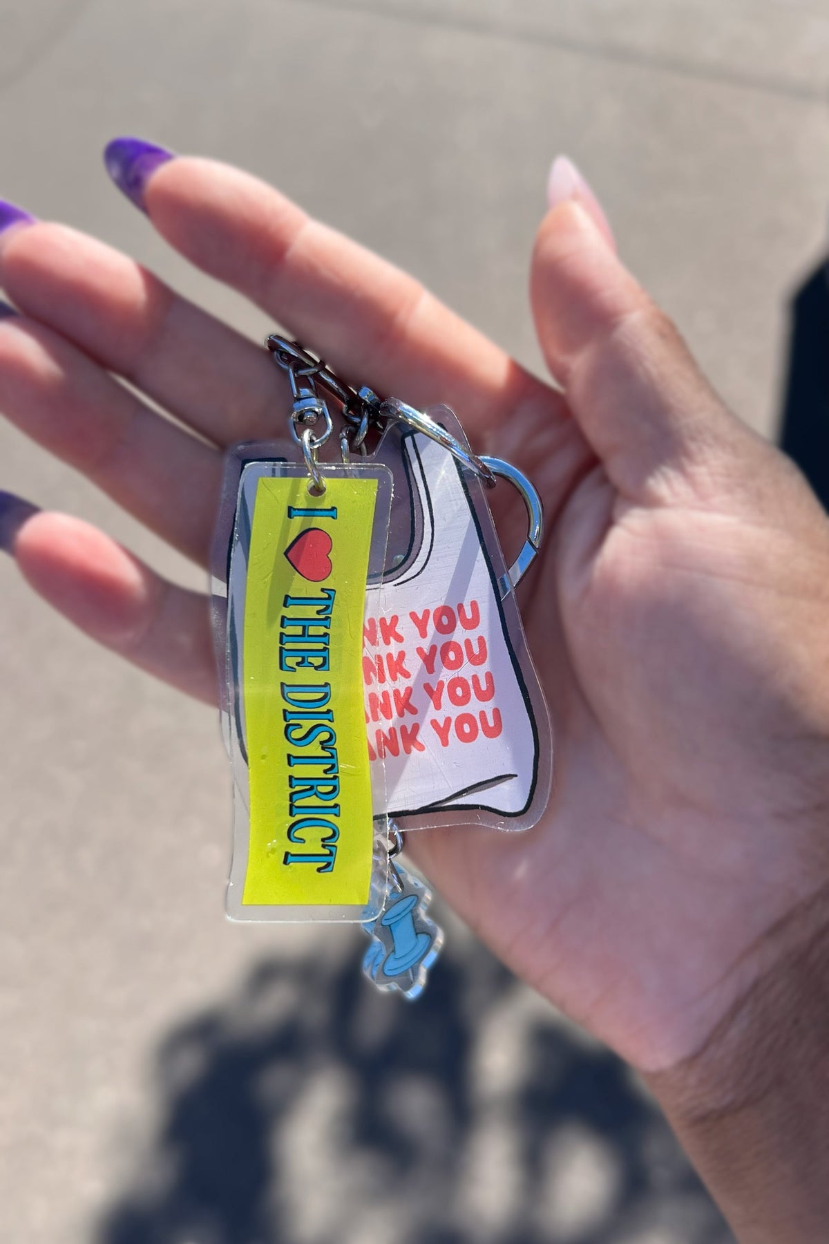Three double-sided clear acrylic keychains, baby blue push pin, thank you takeout bag, and I Love the District keychains. Individual hooks for a layered look and versatile placement.  