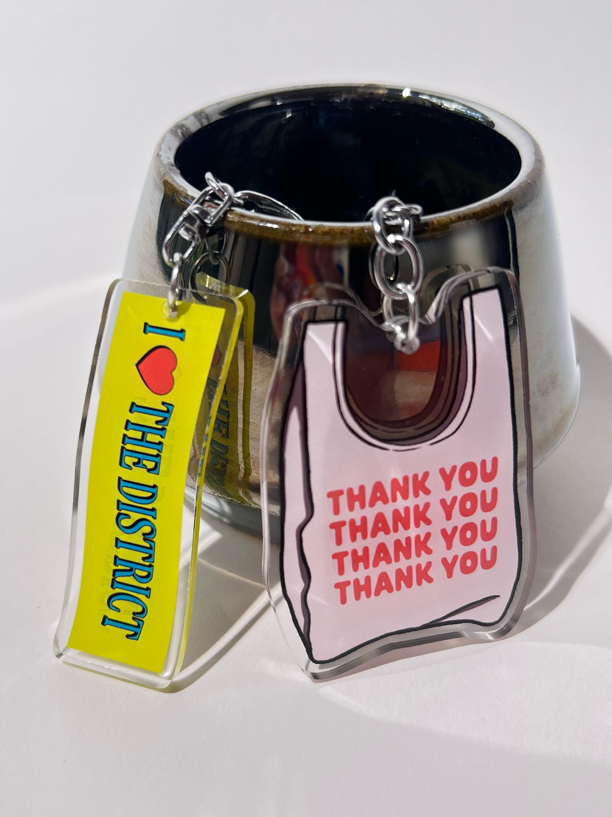 2.5” double-sided clear acrylic keychain featuring an illustrated white takeout bag with vibrant orange-red “thank you” text repeated on the bag. Comes with a lobster clasp, split ring, and chain. Bag charm for totes, crossbody bags, and purses.