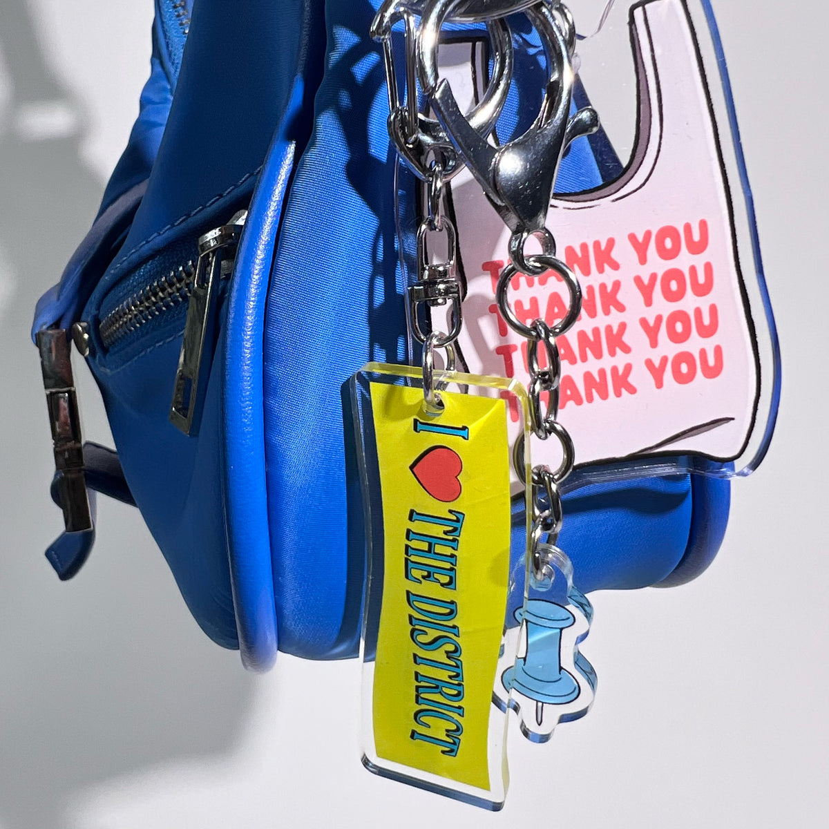 Three double-sided clear acrylic keychains, baby blue push pin, thank you takeout bag, and I Love the District keychains. Individual hooks for a layered look and versatile placement.  