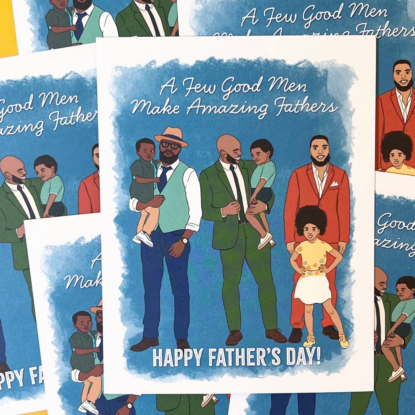4.25 x 5.5” A2 size greeting card illustration of three African American Fathers standing with their kids. Two dads are holding their kid in their arms while another dad stands with his daughter in front of him. Each dad is wearing a suit in blue, green, or terracotta. At the top of the card are the words “A Few Good Men Make Amazing Fathers” with “Happy Father’s Day” at the bottom. The textured watercolor background has shades of blue with a white border.