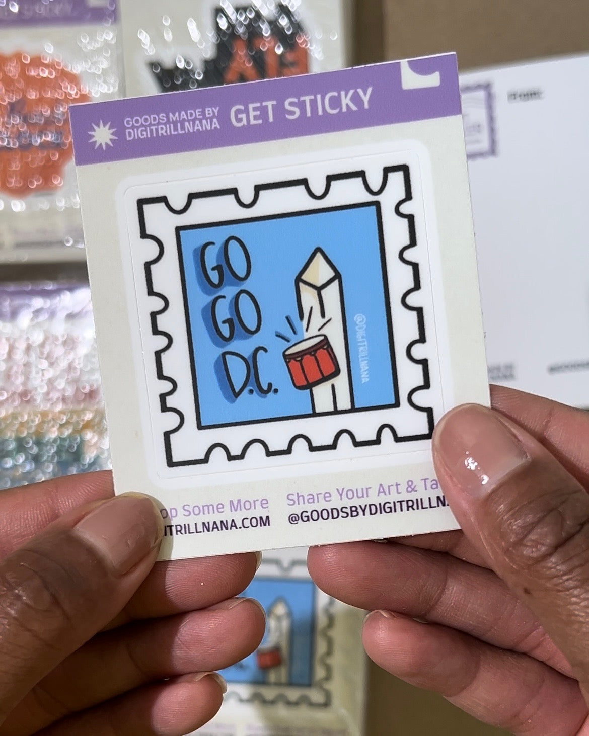 Vibrant postage stamp sticker inspired by Washington DC's Go Go music culture, featuring red drums and the Washington Monument on a light blue background. Includes the words 'Go Go DC'. Ideal for laptops, water bottles, and more!