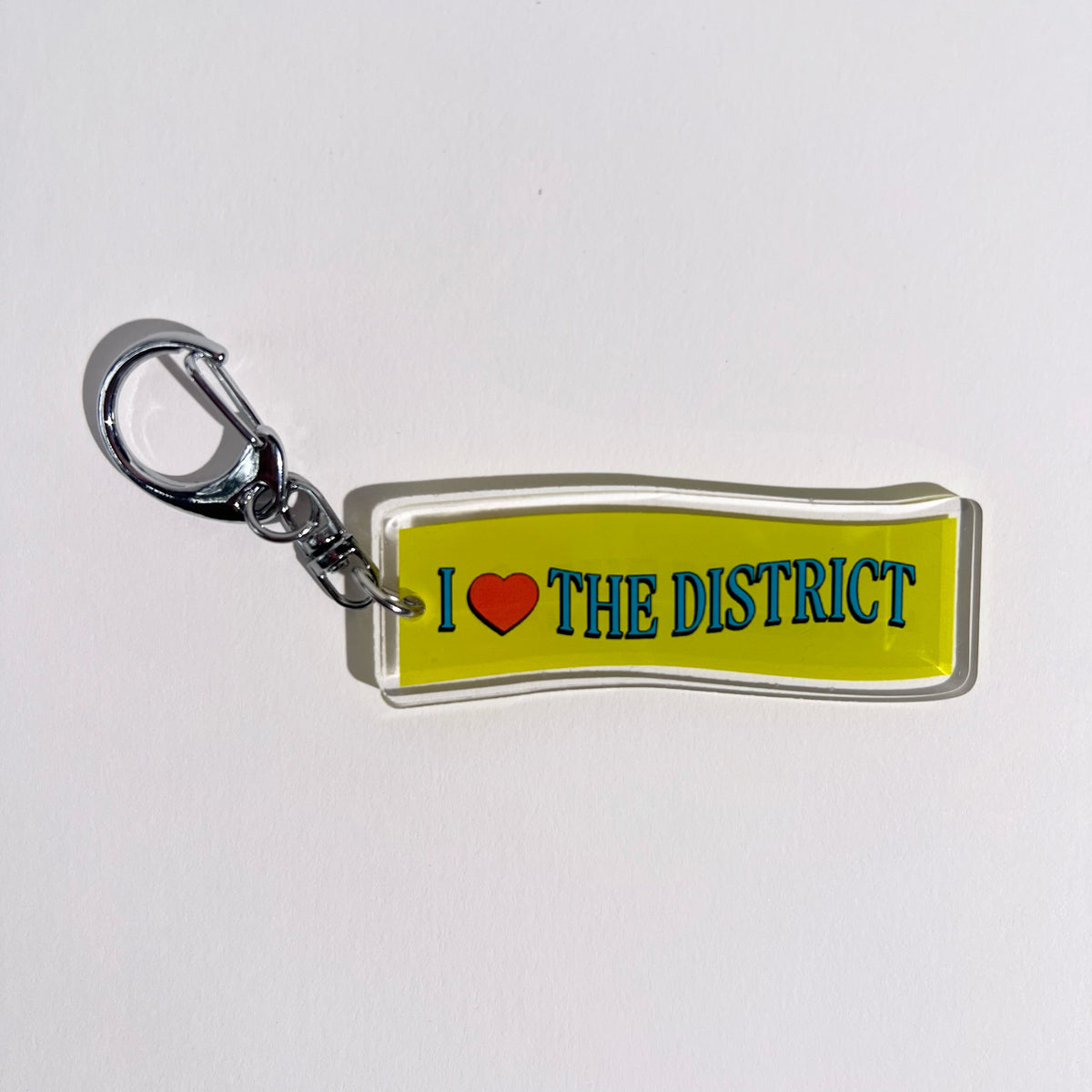 2.5” double-sided clear acrylic keychain with “I ♥ the District” in bright blue and red heart with wave typography treatment on green wave background. Silver D hook clasp and chain. DMV native DC Maryland Virginia bag charm for totes and crossbody bags. Washington DC hometown souvenir. 