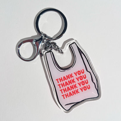 2.5” double-sided clear acrylic keychain featuring an illustrated white takeout bag with vibrant orange-red “thank you” text repeated on the bag. Comes with a lobster clasp, split ring, and chain. Bag charm for totes, crossbody bags, and purses.